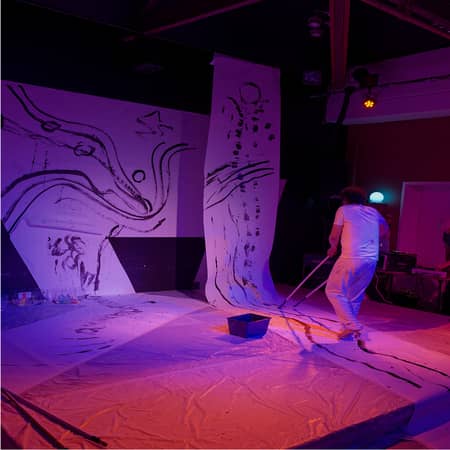 photo de Diego qui performe en peignant en noir sur de grandes bandes de papier blanc au sol